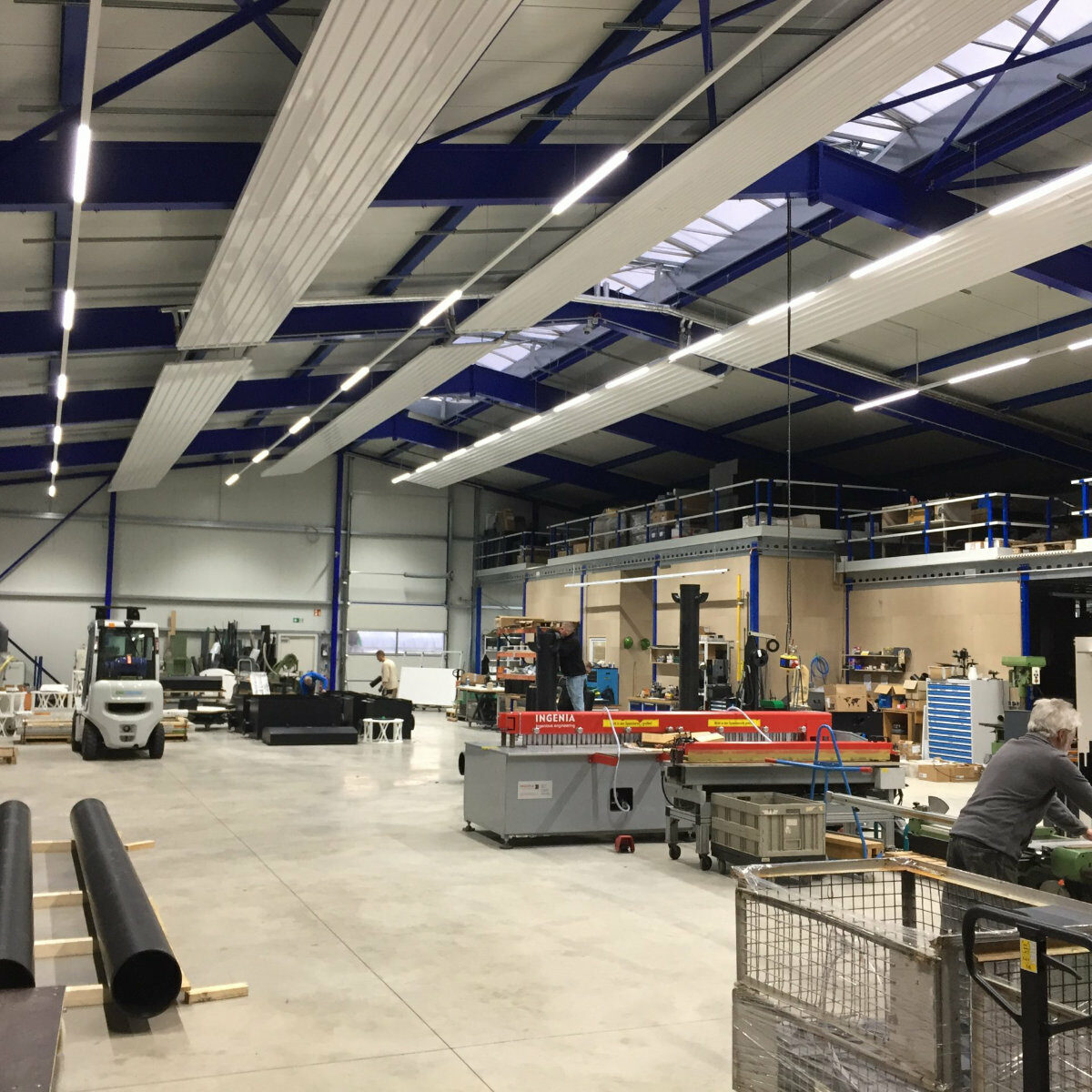 Moderne helle Lagerhalle in der mehrere Personen an Maschinen arbeiten.