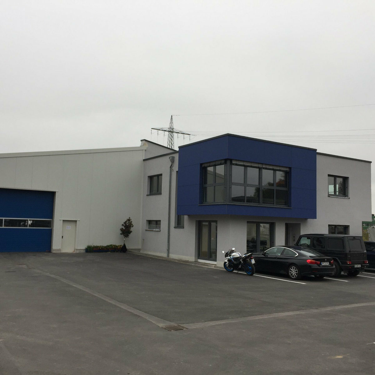 Weiße Lagerhalle vor der mehrere Fahrzeuge stehen.