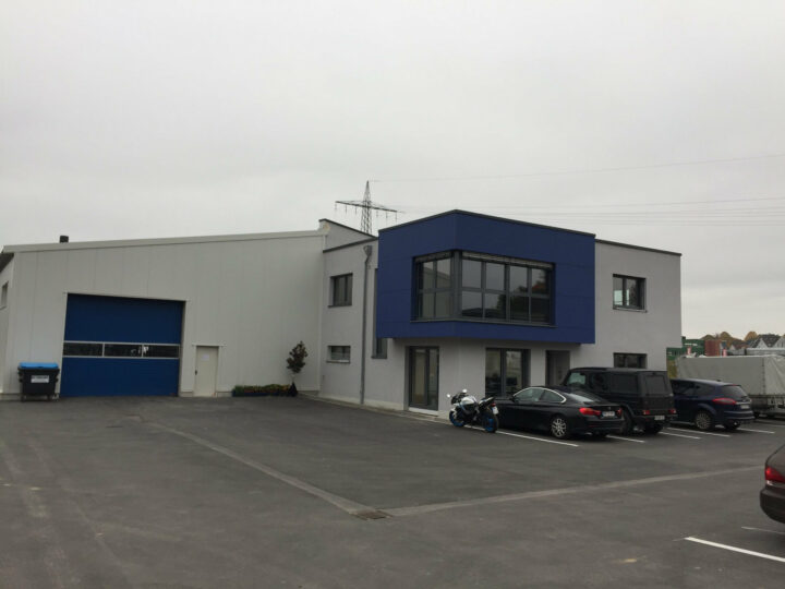 Weiße Lagerhalle vor der mehrere Fahrzeuge stehen.