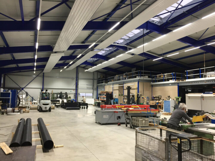 Moderne helle Lagerhalle in der mehrere Personen an Maschinen arbeiten.