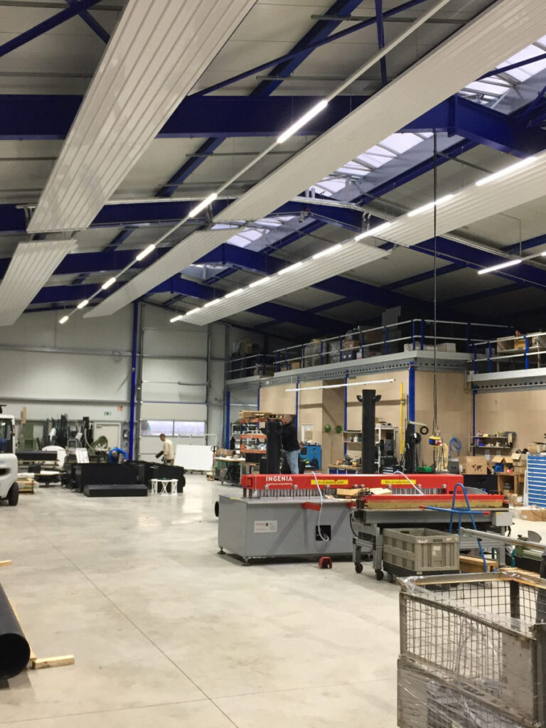 Moderne helle Lagerhalle in der mehrere Personen an Maschinen arbeiten.