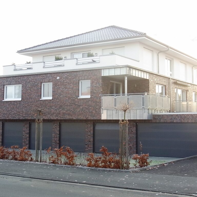 Mehrfamilienhaus mit dunklem Klinker und weißen Fenstern.