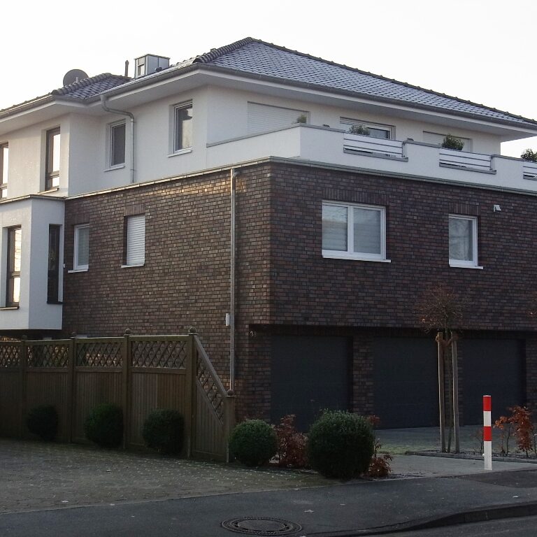 Mehrfamilienhaus mit dunklem Klinker und weißen Fenstern.