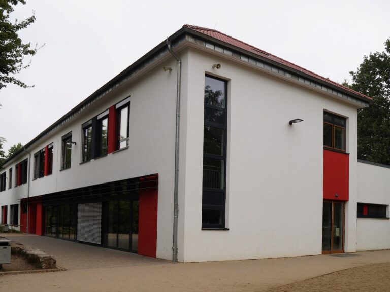 Weiß verputztes Gebäude mit roten Akzentflächen.