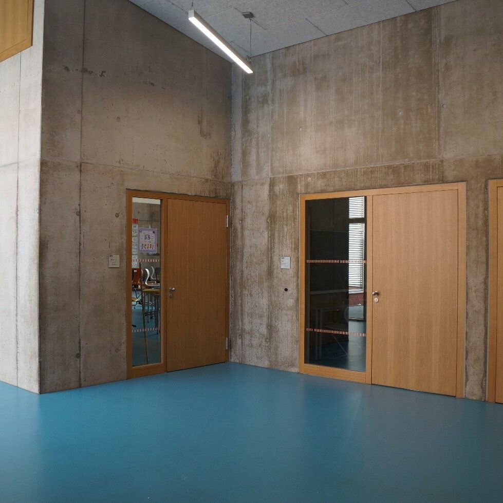 Flur mit drei Türen, blauem Boden und Betonwänden.