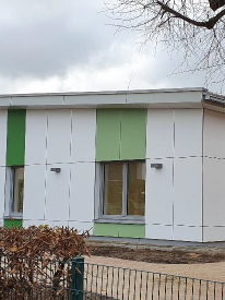 Weißes einstöckiges Gebäude mit Flachdach und farbigen Flächen über den Fenstern in verschiedenen Grüntönen.