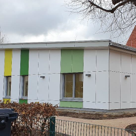 Weißes einstöckiges Gebäude mit Flachdach und farbigen Flächen über den Fenstern in verschiedenen Grüntönen.