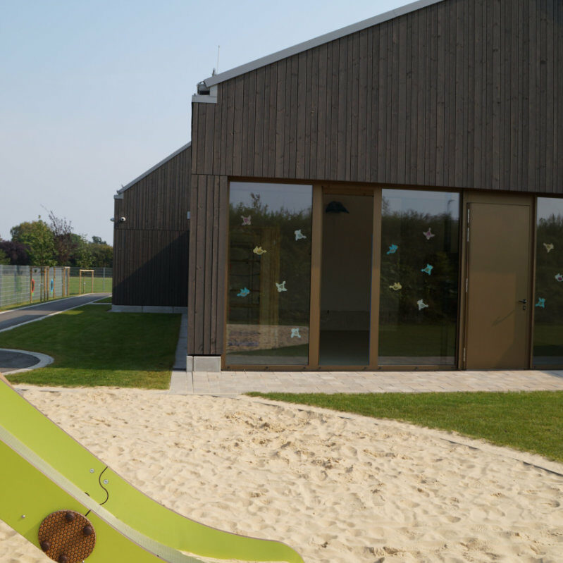 Kitagebäude mit grüner Rasenfläche und Spielplatz.