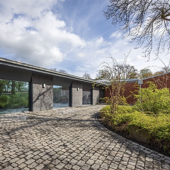 Einstöckiger Flachdachbau mit dunklem Klinker und gepflastertem Weg.