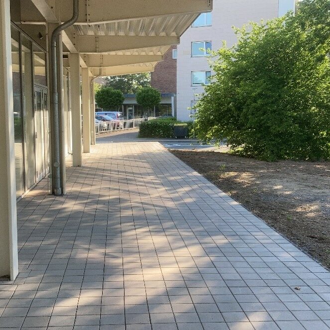 Gepflasterter Weg unter Abdach neben Fensterfront.