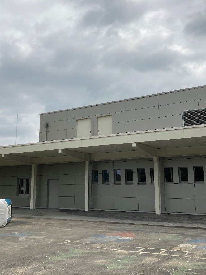 Graues Gebäude mit kleinen Fenstern und langem Abdach.