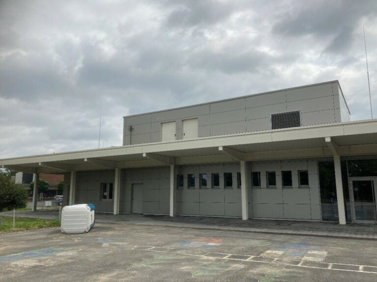 Graues Gebäude mit kleinen Fenstern und langem Abdach.