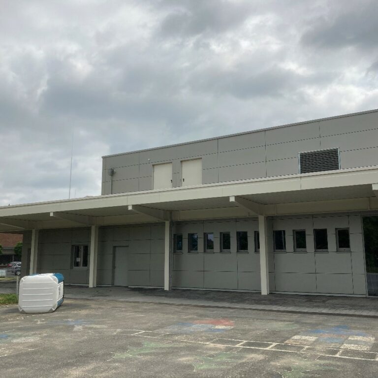 aig-mensa-kamp-lintfort2 Graues Gebäude mit kleinen Fenstern und langem Abdach.