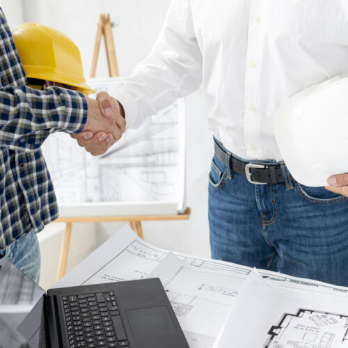 Zwei Männer in Hemd und Bauhelm in der Hand geben sich die Hände.