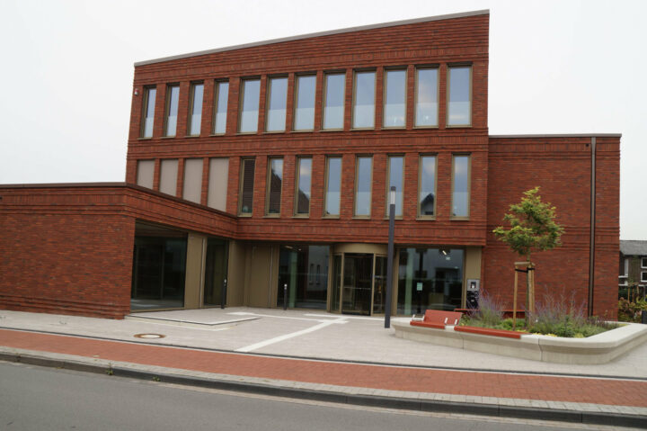 Rotes mehrstöckiges Backsteingebäude mit gepflastertem Eingangsbereich.