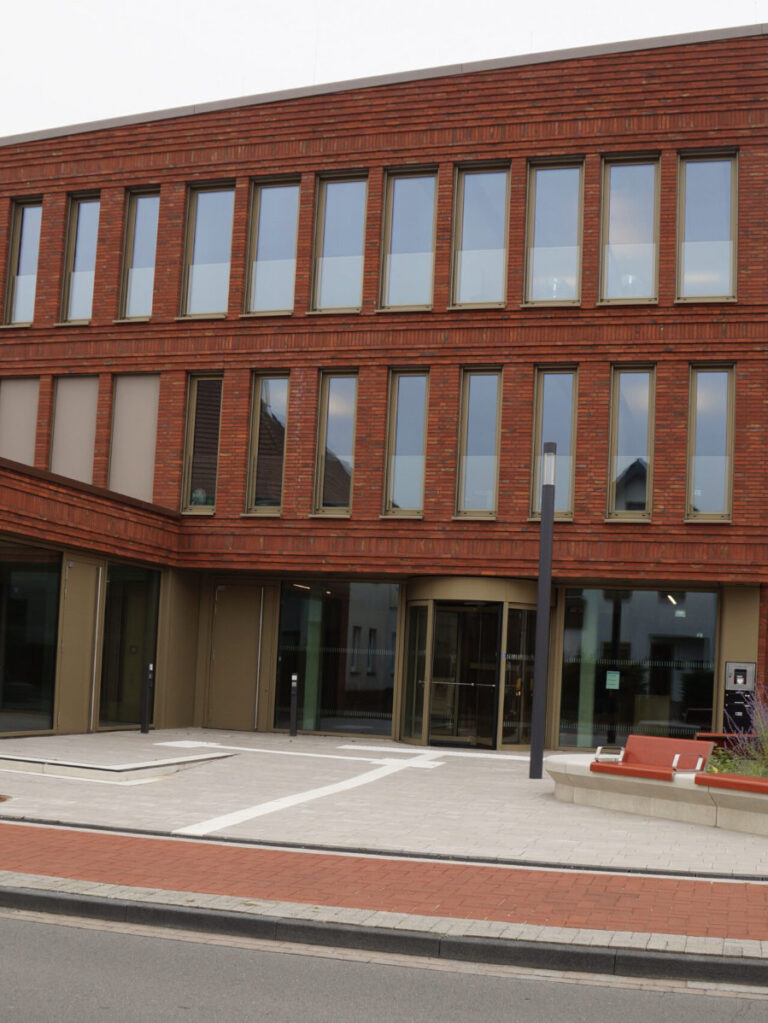 Rotes mehrstöckiges Backsteingebäude mit gepflastertem Eingangsbereich.