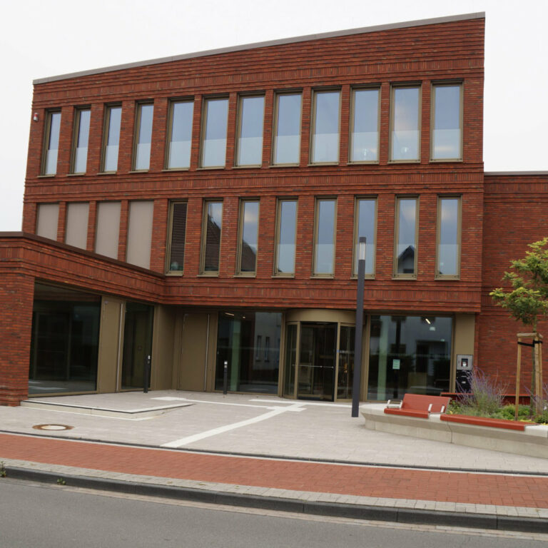 Rotes mehrstöckiges Backsteingebäude mit gepflastertem Eingangsbereich.