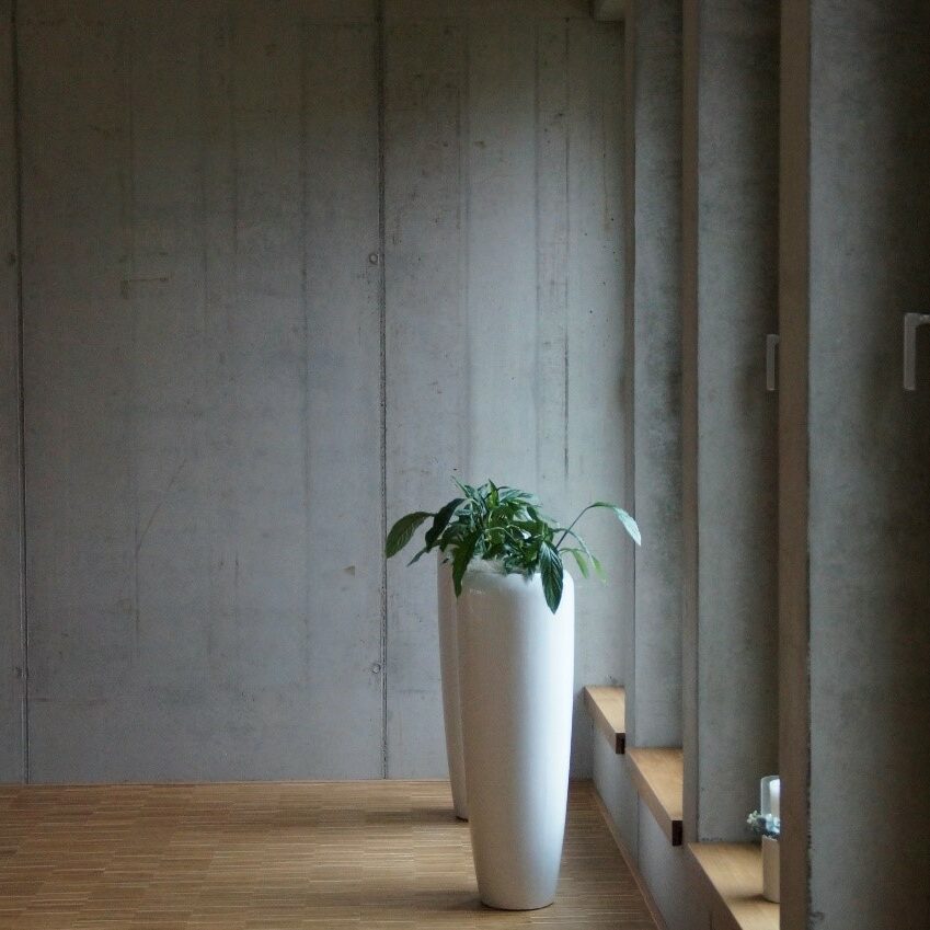 Zwei weiße Vasen auf Holzboden vor Betonhintergrund.