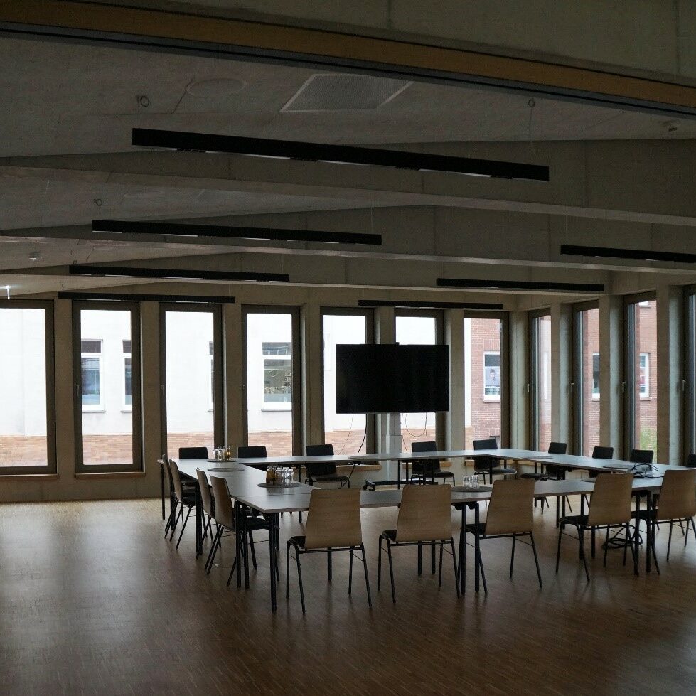 Besprechungsraum mit rundangeordneten Tischen und Stühlen vor einem Fernseher.