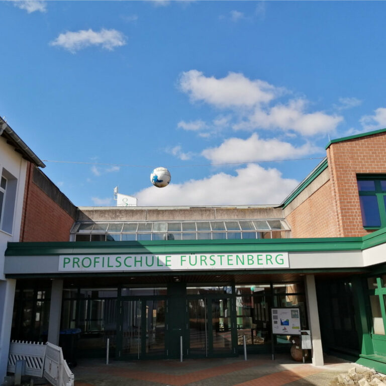 aig-schulzentrum-fuerstenberg Rotes Backsteingebäude mit grünen Fenstern und der Aufschrift Profilschule Fürstenberg.