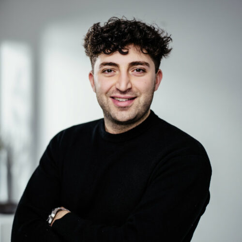 Junger Mann mit zerzausten braunen und schwarzem Pullover lächelt freundlich