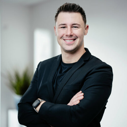 Großer Mann in schwarzer Businesskleidung verschränkt die Arme und lächelt freundlich