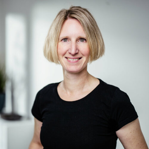 Frau mit kurzen blonden Haaren und schwarzem T-Shirt lächelt freundlich