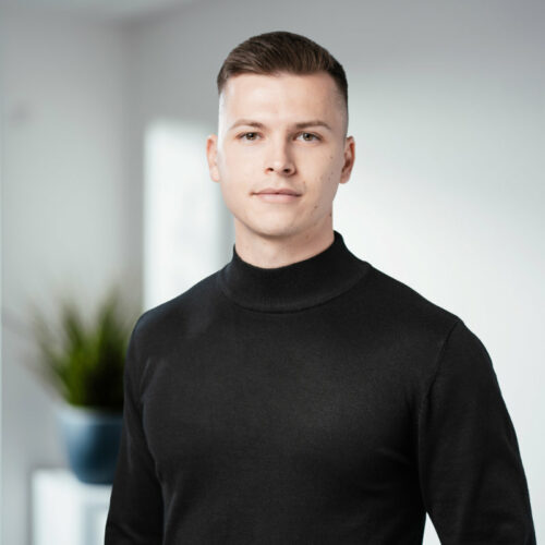 Dünner Mann mit dunkel-blondem Haar und dunklem Kragenpullover lächelt